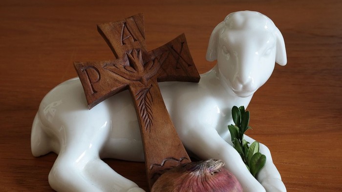 Weißes Lammfigürchen mit Kreuz und Zwiebel auf Holzoberfläche