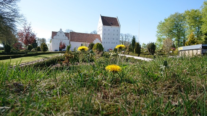En stor, hvid bygning med røde tag og en mur med guldåg i forgrunden