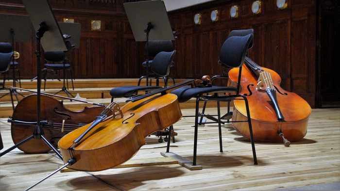 To celler og en kontrabas på stoler i koncertsal