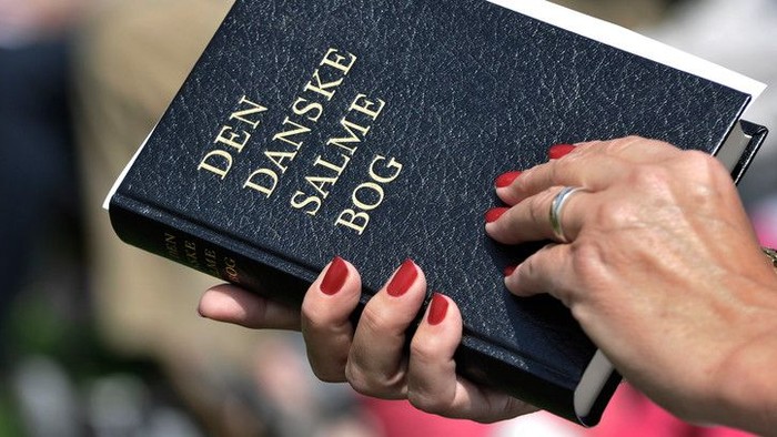 En person holder en Dansk Salmebog.