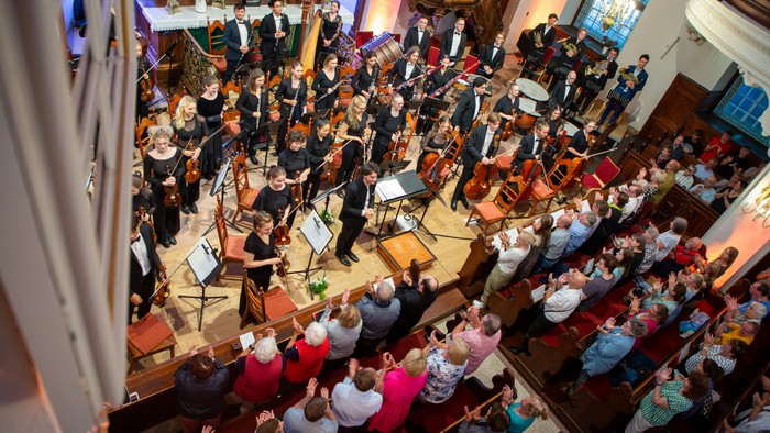 Ein Orchester spielt in einem großen Saal vor einem Publikum.