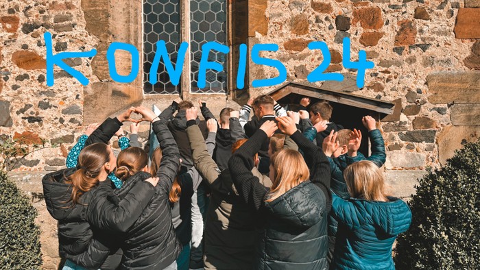 Gruppe von Personen, die vor einem Steingebäude mit einem Schild mit der Aufschrift „KONFIS 24“ für ein Foto posieren.