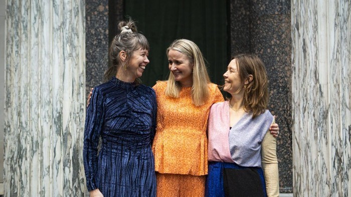Tre kvinder står sammen og smiler til kameraet.