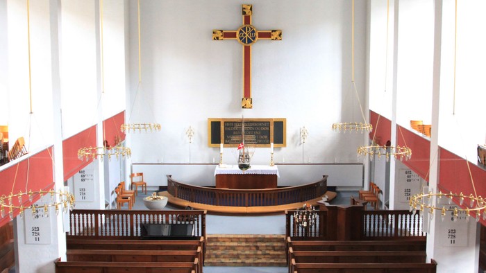 Indre del af kirke med alter, kors og bænke.