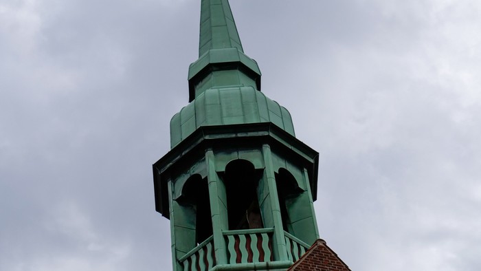 Grøn kirketårn med spire og vejer på rødt tag.