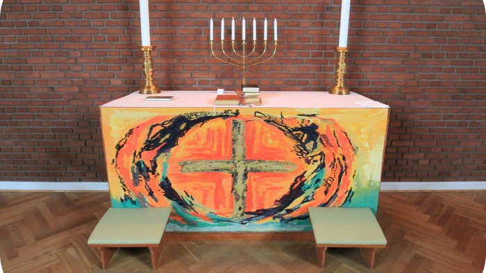 Altaret i kirken med farverig dækkede bord og to benker foran