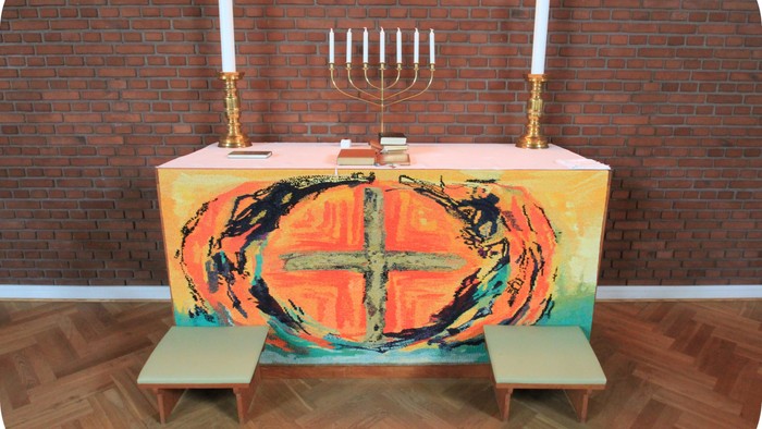 Altaret i kirken med farverig dækkede bord og to benker foran