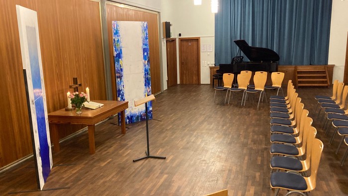 Ein geräumiger Raum mit Holzbestuhlung für eine Veranstaltung, ausgestattet mit einem dekorierten Altar und einer Bühnenrückwand.