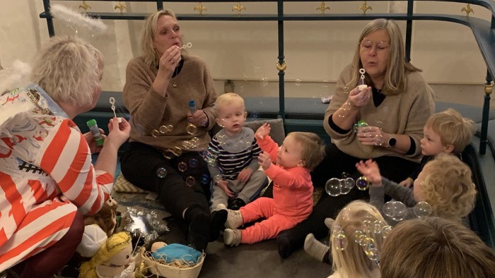 En gruppe børn og voksne sidder på gulv og blæser boble.