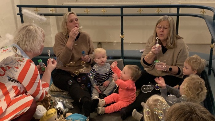 En gruppe børn og voksne sidder på gulv og blæser boble.
