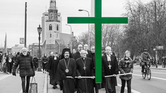Eine Gruppe von Priestern trägt ein großes grünes Kreuz durch eine Stadt.