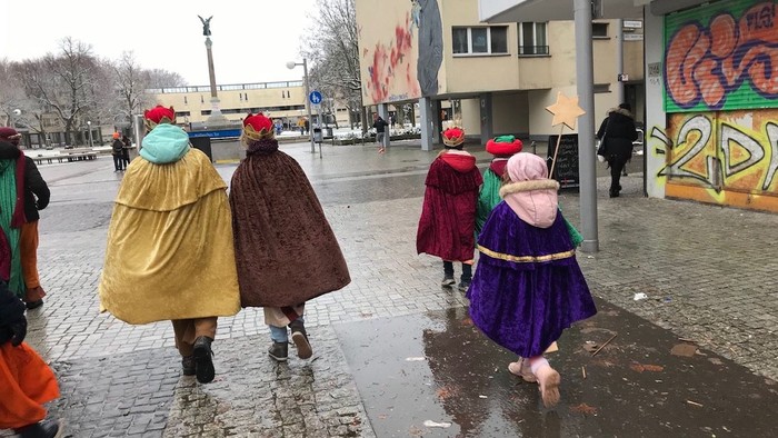 Kinder in Kostümen, die auf einer regennassen Straße gehen.