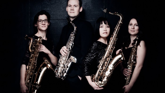Vier Musiker posieren mit ihren Saxophonen vor dunklem Hintergrund