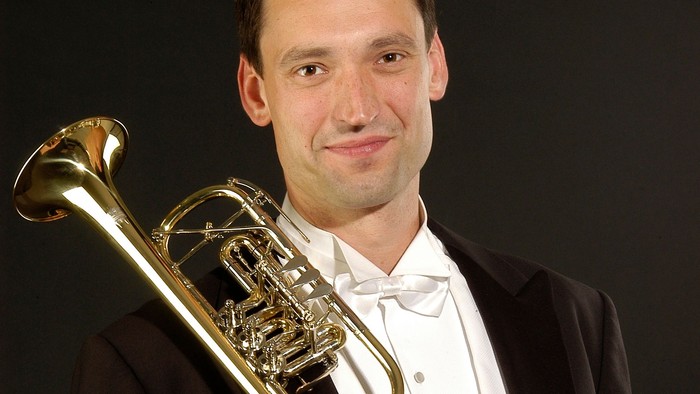 Ein Mann in Anzug hält eine Posaune