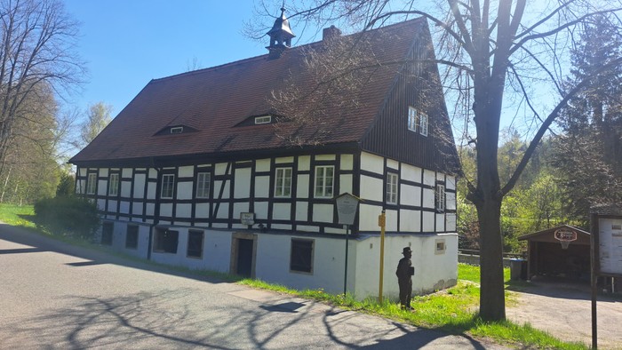 Das Bild zeigt ein traditionelles Fachwerkhaus mit einem Mann davor.