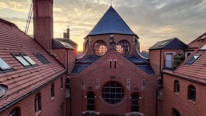 Ein rotes Backsteingebäude mit spitzen Dach und Rundbogenfenstern bei Sonnenuntergang