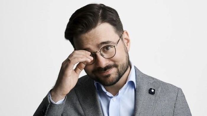 Mand i grå suite og blå skjorte justerer brillerne.