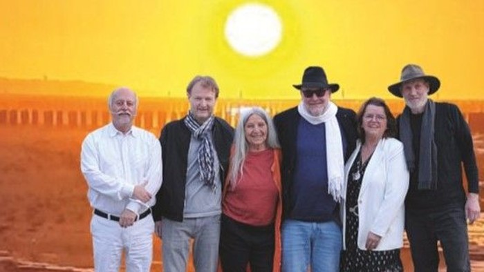 Eine Gruppe von sechs Personen posiert vor einer untergehenden Sonne in der Wüste