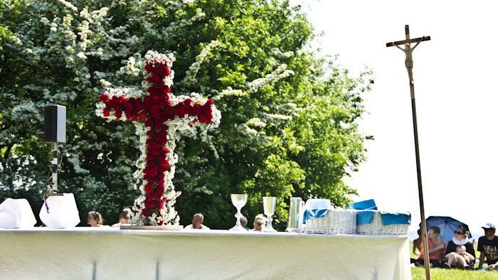En stor rød kransformet i et kors på en festtabell med blomster og drikkeglasker.