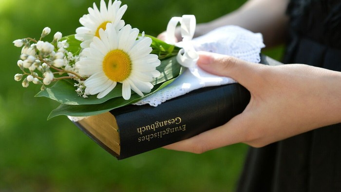 Eine Hand hält ein Buch mit einer weißen Blume darauf