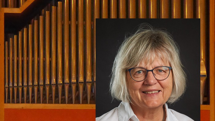 En kvinde med blondt hår og briller sidder ved et orgel.