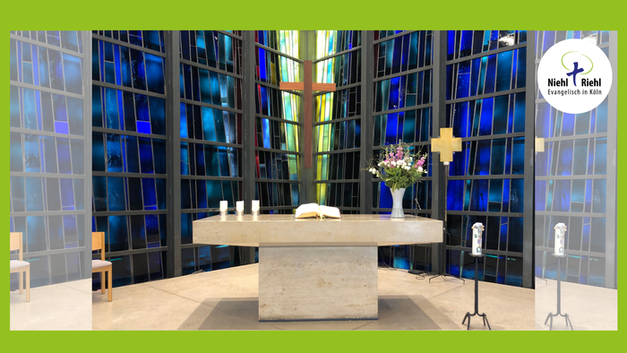 Moderne Kirche mit großem Glasfenster und Altar mit Blumen.
