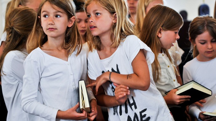 En gruppe børn i hvide t-shirts holder håndskrevne skilt.