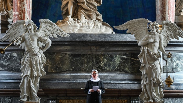 En præst står i en prægtig kirke med store skulpturer og billeder af engle.