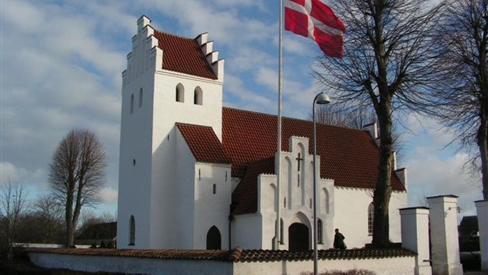 En hvid kirke med røde tag og en dansk flag på en stang foran.