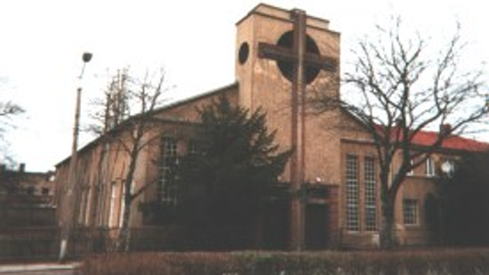 Das Bild zeigt eine Kirche mit einem Glockenturm und Bäumen davor.