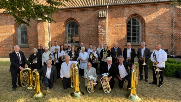 En gruppe musiker poserer med instrumenter i forgrunden af en kirke