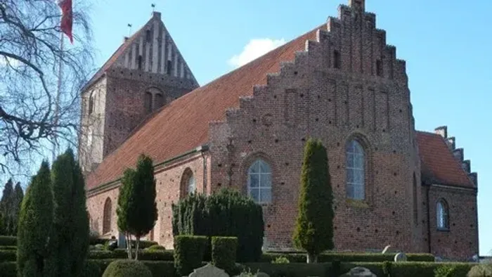 Gamle teglkirke med spire og vinduer, omgivet af grønne træer og buske