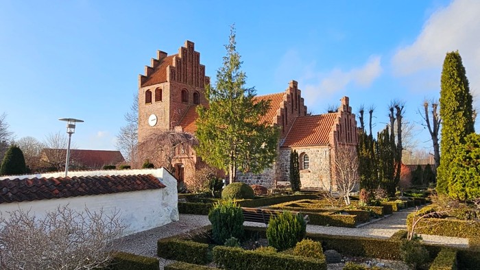 En smuk have med formede hegn og en stor kirke i baggrunden