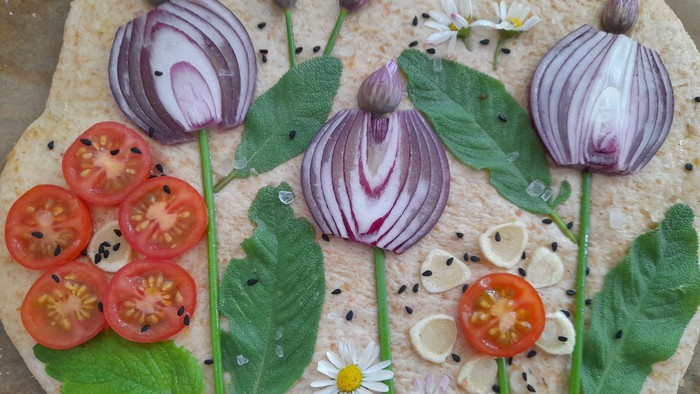 Ein selbstgemachter Pizzateig mit Gemüse und Kräutern in Form von Blumen und Blättern.