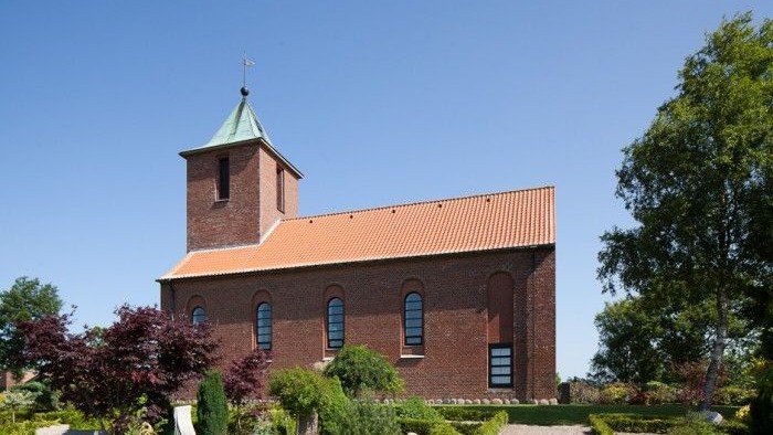 En rød murstenskirke med tårn og grønne træer.