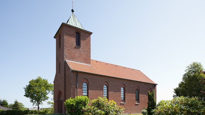 Røde kirke med tårn og spids tak i grønne omgivelser