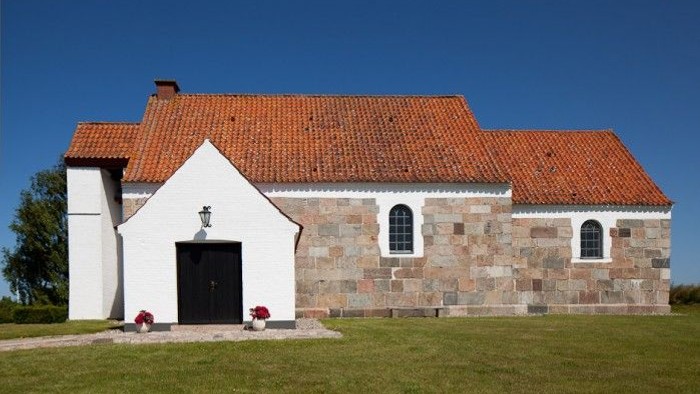 En lille kirke med røde tag og murstensmurer, beliggende på en grøn eng.