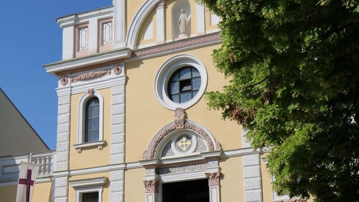Gelbe Kirche mit weißem Portal und Rundfenster.
