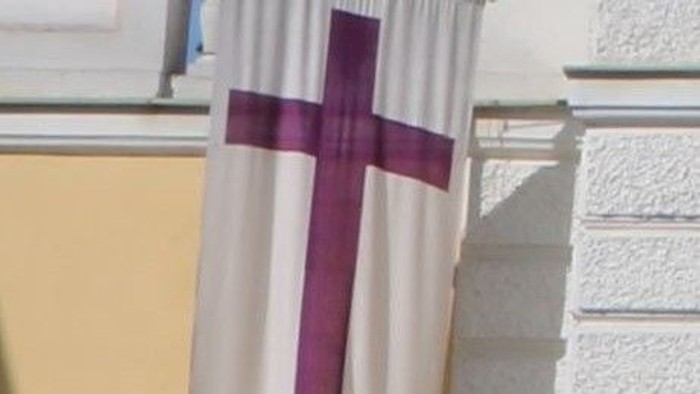 Ein weißes Tuch mit lila Kreuz vor einem Gebäude.