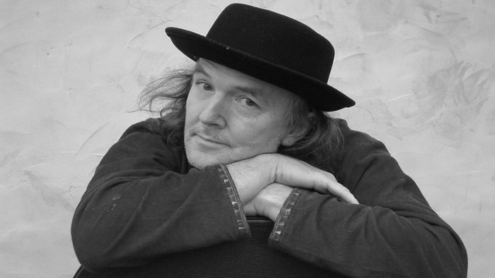 Ein Mann mit Hut und langer Mähne schaut nachdenklich.