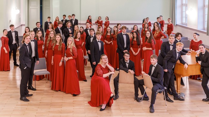 Eine Gruppe von Menschen in roten Kleidern und schwarzen Anzügen posiert in einem Raum