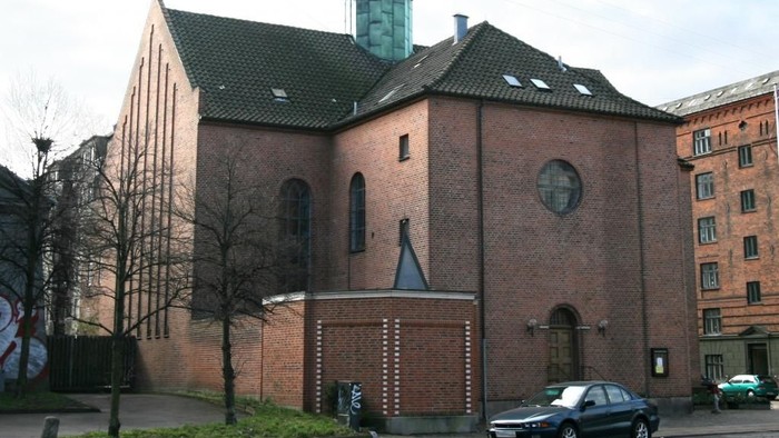 En rød murstenskirke med tårn og grøn tag.