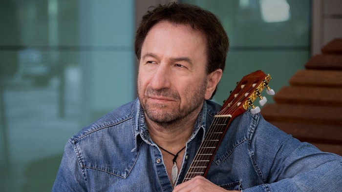 Ein Mann hält eine Gitarre und lächelt.