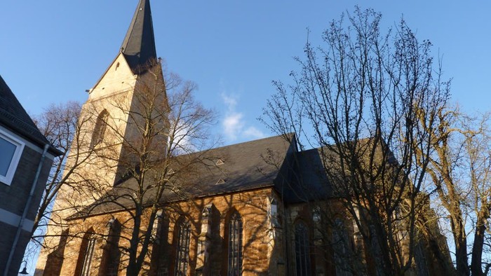 Kirche mit hohem Kirchturm und Rundbogenfenstern, umgeben von Bäumen.