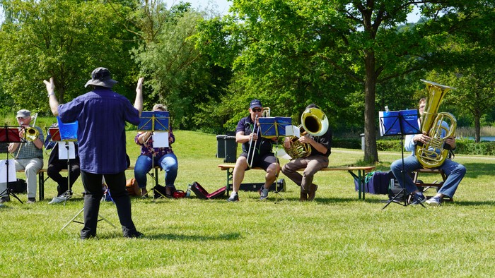 Eine Band probt im Freien mit einem Dirigenten, der sie anführt.