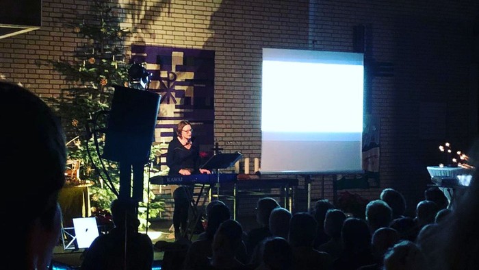 Eine Frau spricht vor einem Publikum vor einem Gebäude mit einem Bildschirm.