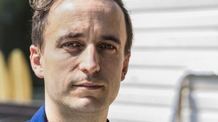 Ein Mann mit kurzem Haar und blauer Jacke schaut ernst in die Kamera.