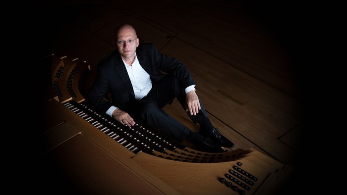 Ein Mann in Anzug sitzt auf einem großen Klavier.