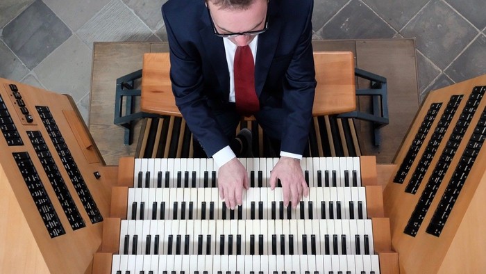 Mann in Anzug spielt auf einem großen Kirchenorgel.