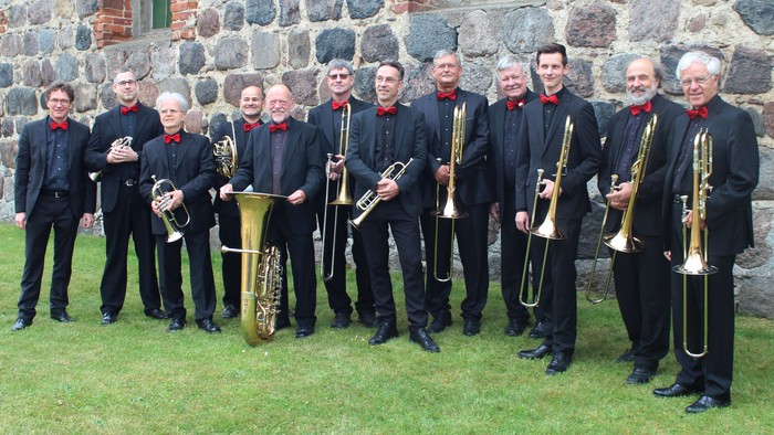 Eine Gruppe von Musikern posiert vor einer Steinmauer, jeder hält ein Blasinstrument